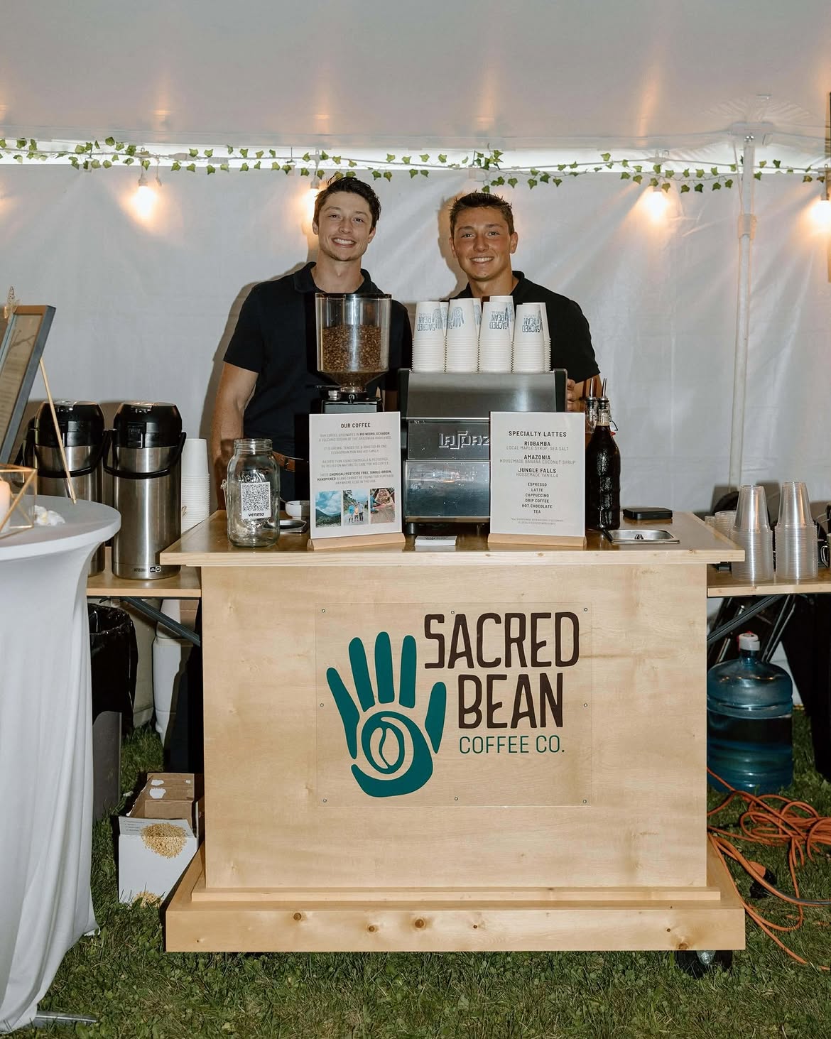 Sacred Bean espresso cart with two baristas at a tented event
