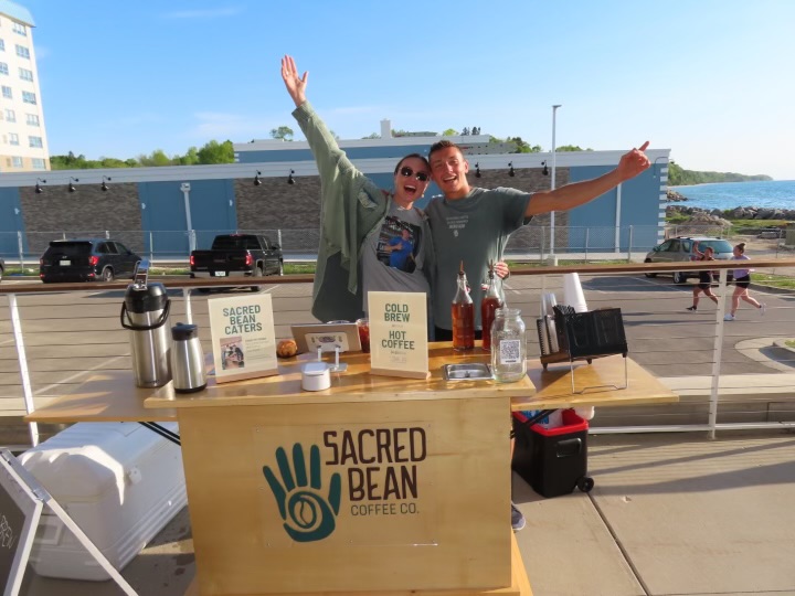 Two Sacred Bean baristas cheering behind the cart with Lake Michigan in the background