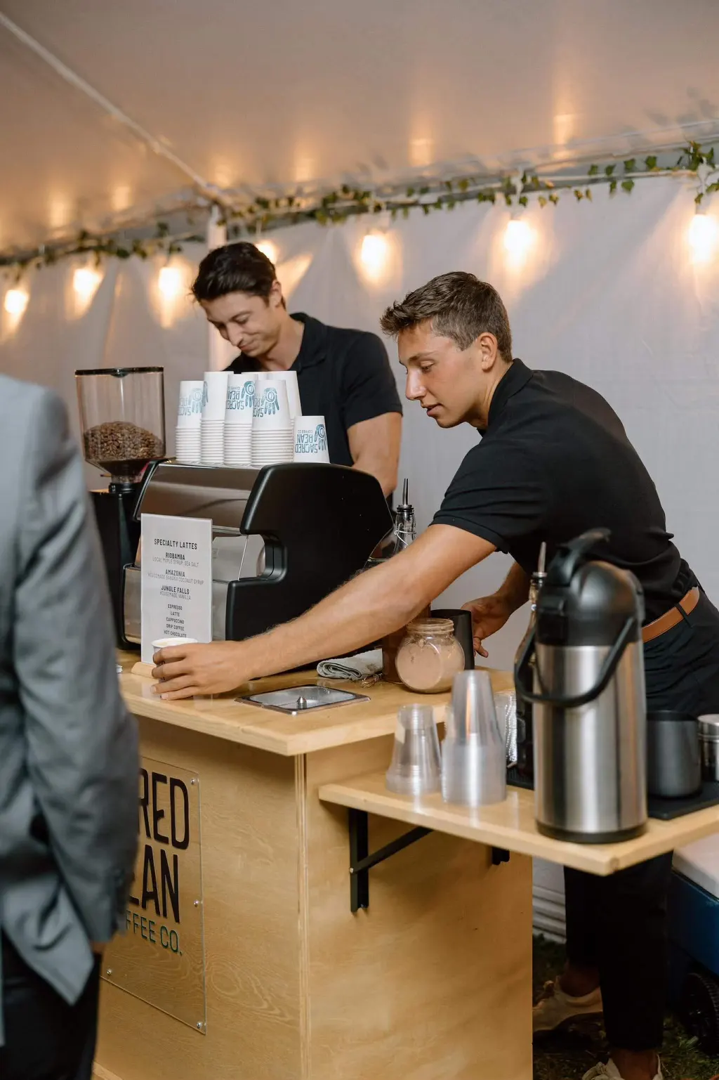 Two Sacred Bean baristas working the espresso cart at a tented evening event